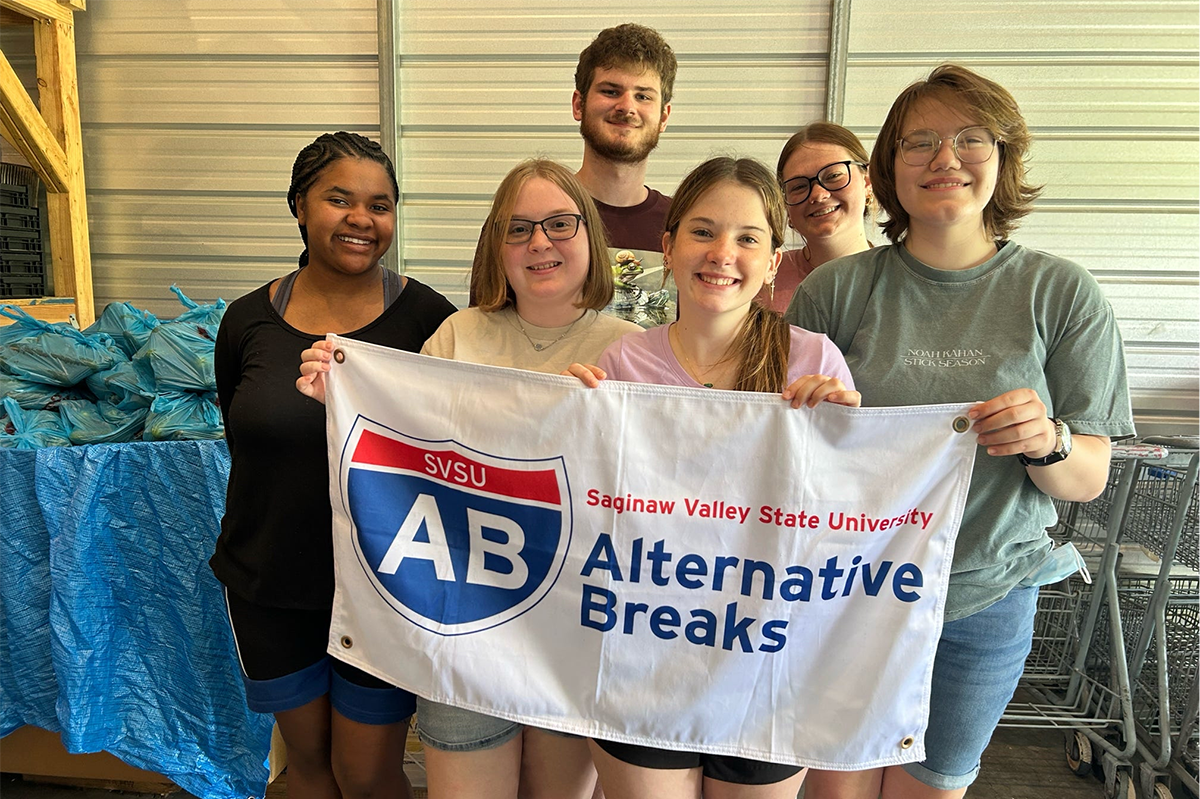 Group of six young adults holding Alternative Breaks flag